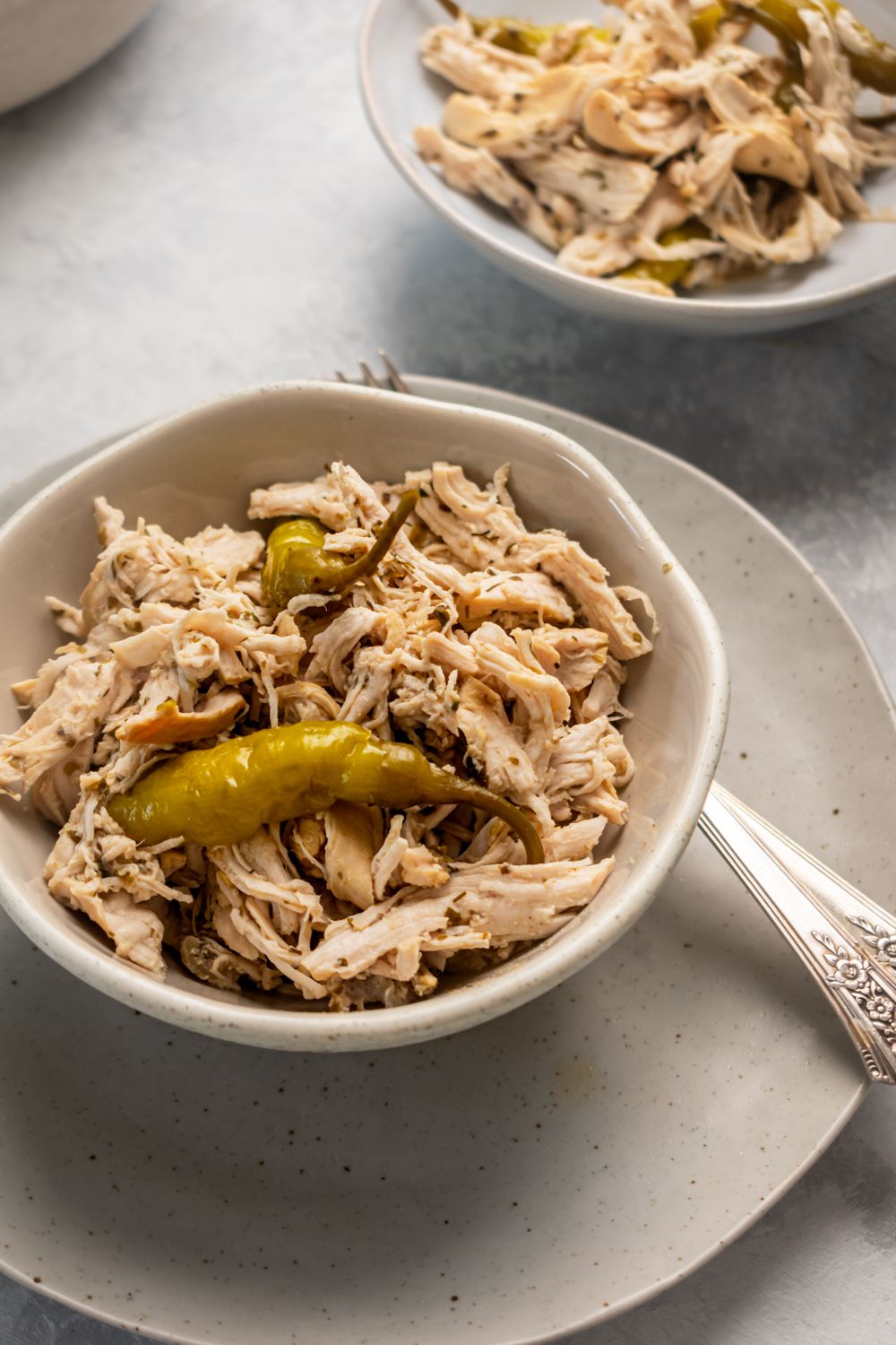 Slow cooker chicken breast with pepperoncini peppers in a bowl with Italian seasoning.