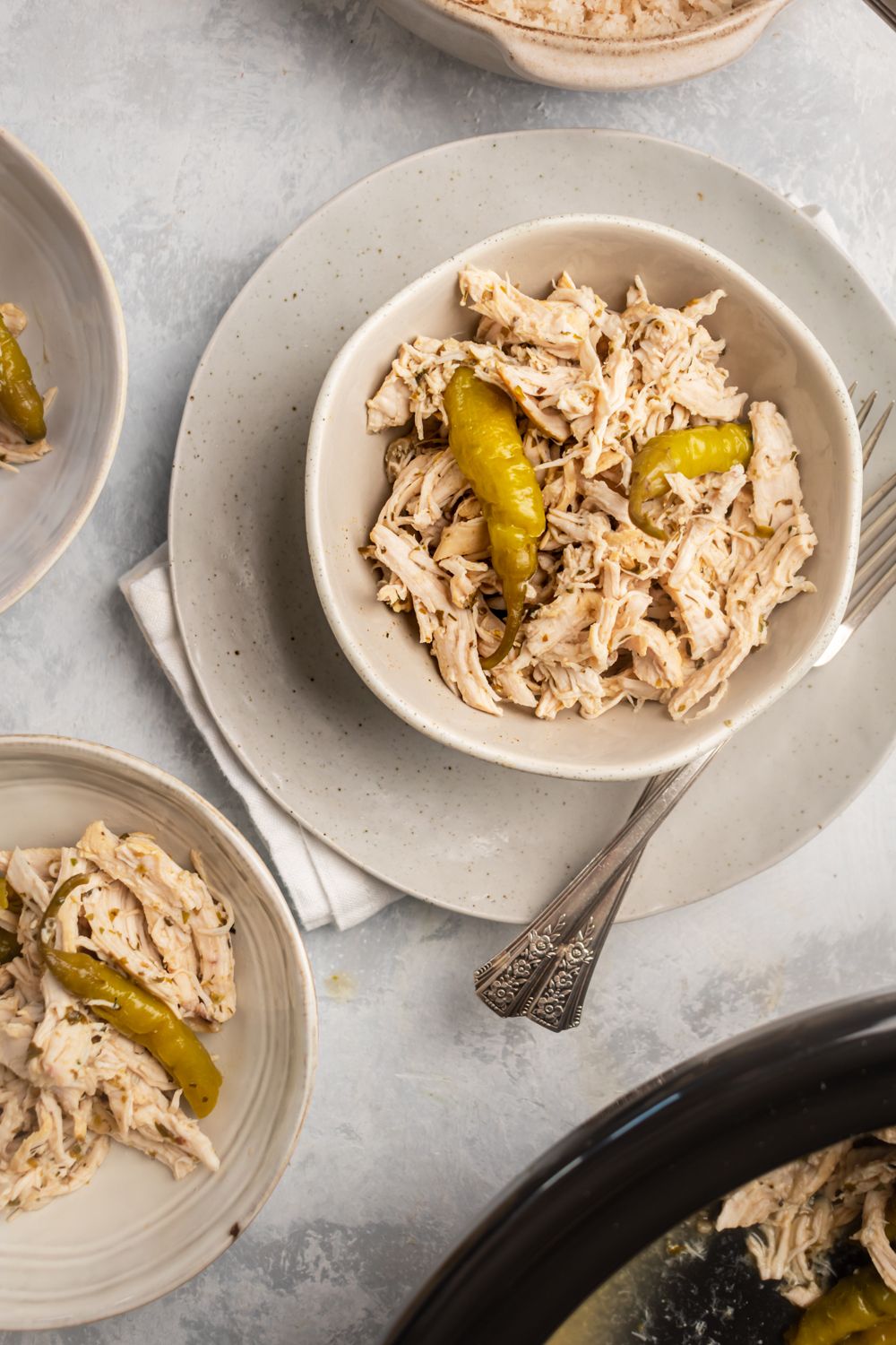 Pepperoncini chicken breast cooked in the slow cooker and then shredded in a bowl with whole pepperoncini peppers.
