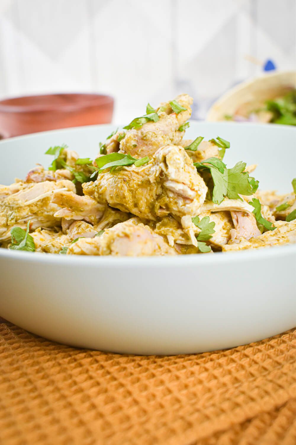 Crockpot salsa chicken with green salsa shredded in a bowl with red onions and cilantro.