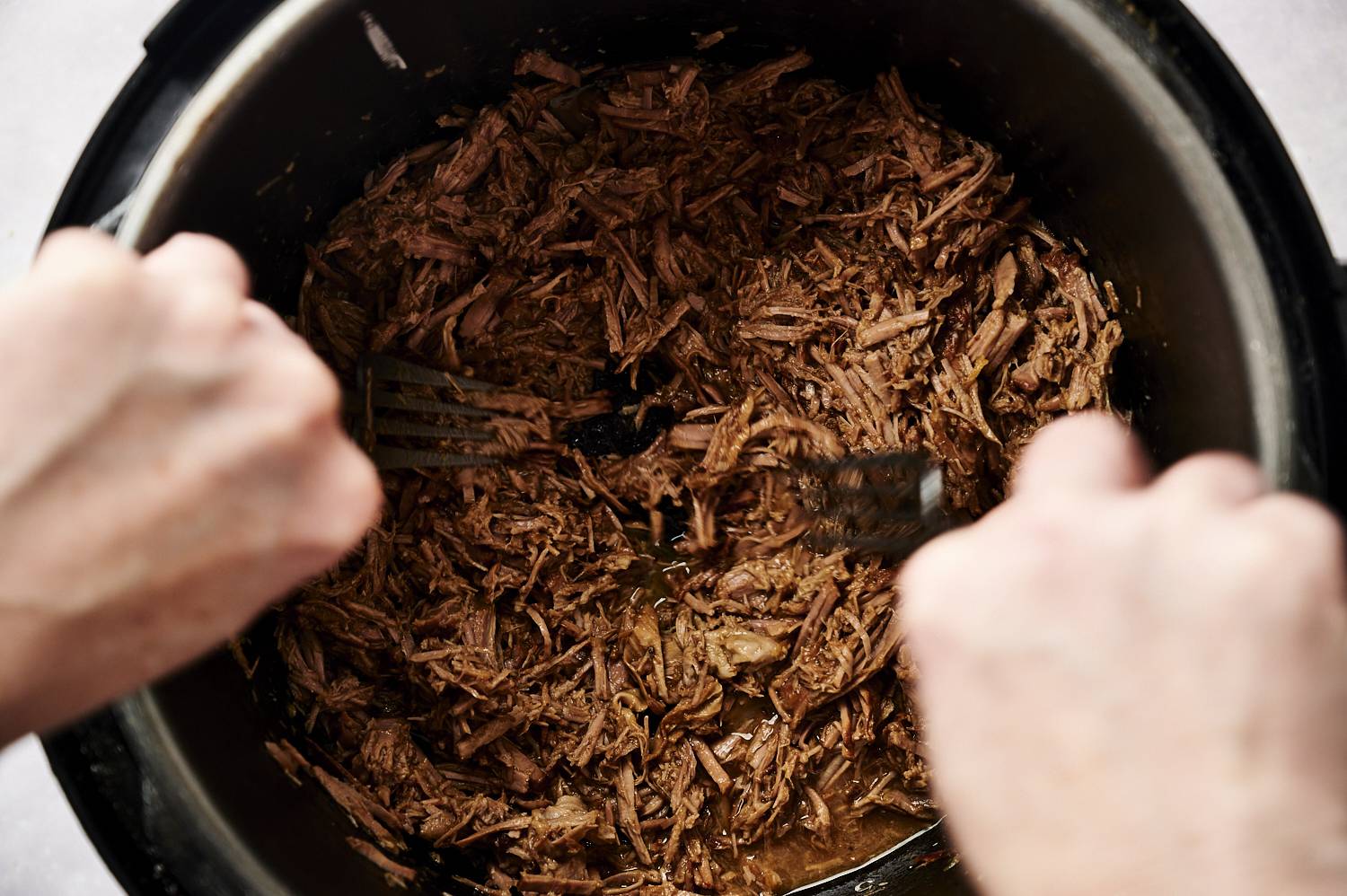 Shredding tender sesame beef in the slow cooker with forks.