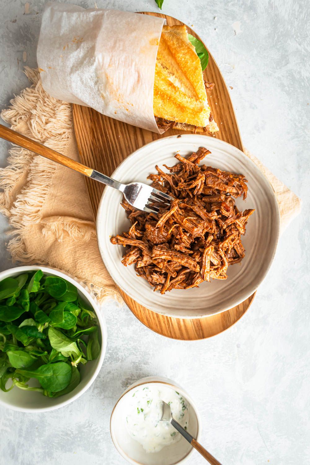Shredded Italian beef served in a bowl and as a sandwich on a wooden board.
