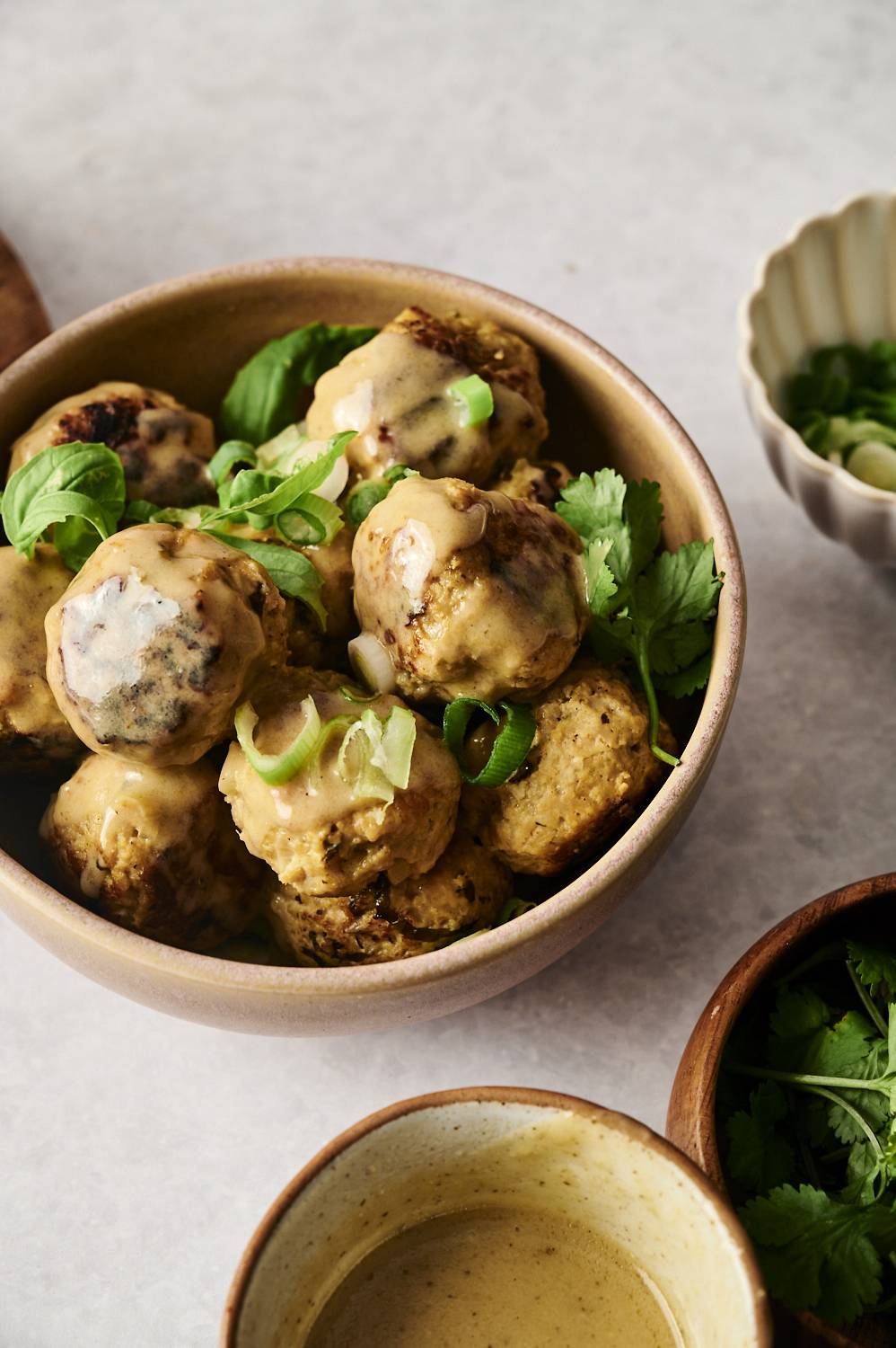 Bowl of Thai curry chicken meatballs topped with creamy sauce, green onions, and fresh herbs.