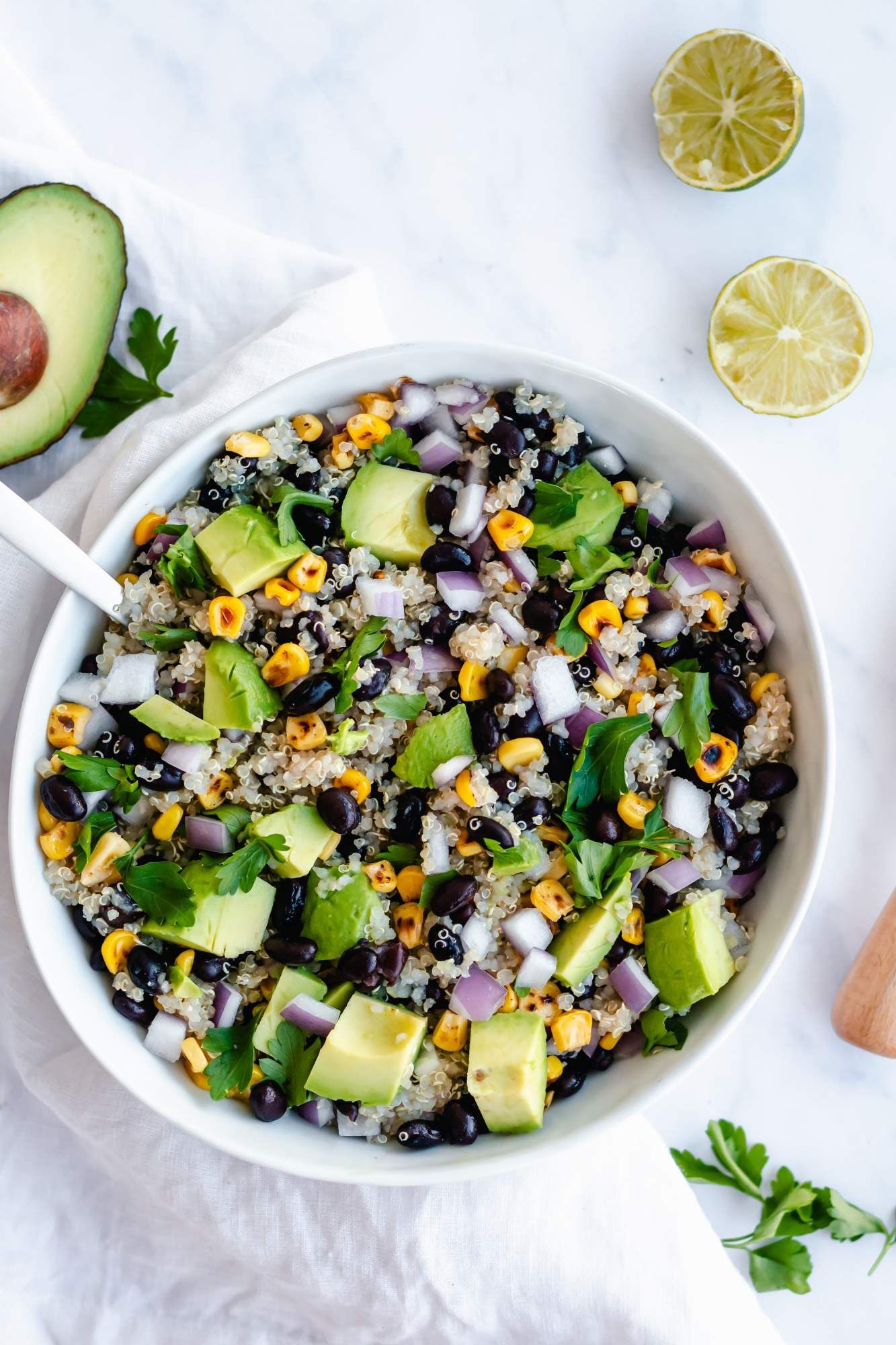 Black bean and quinoa salad with avocado, cilantro, corn, and red onion in a bowl with limes on the side.