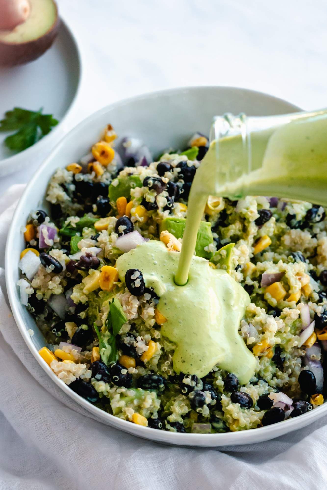 Avocado cilantro dressing being poured on a quinoa and black bean salad in a white bowl.