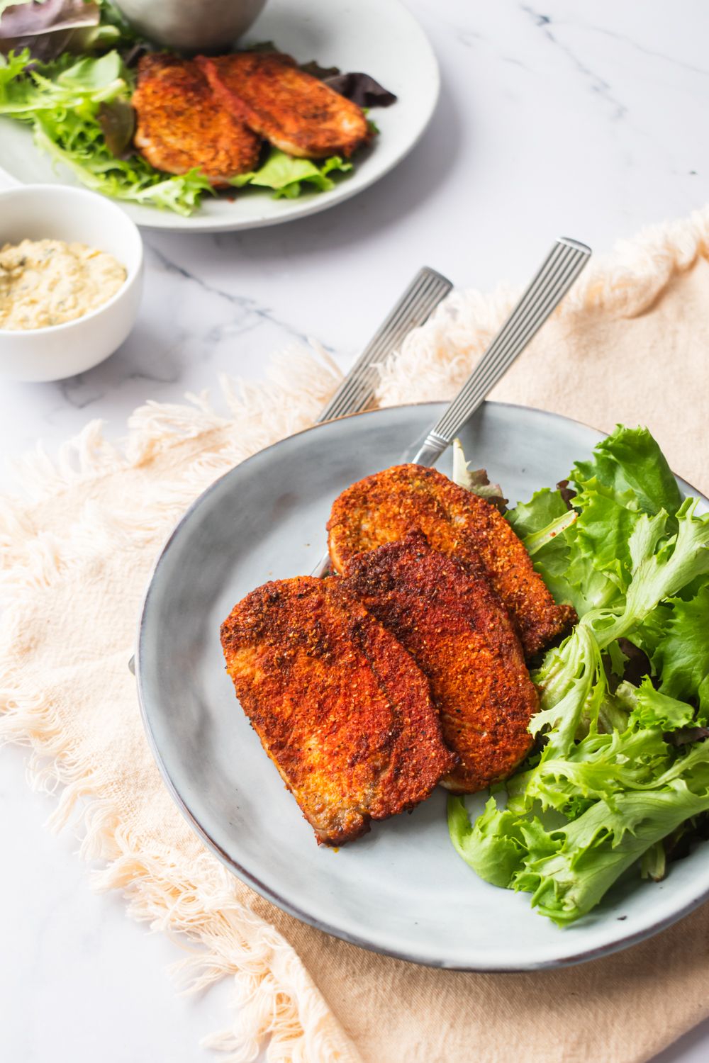 Pork chops with a spice crust on a plate with green salad on a yellow napkin.
