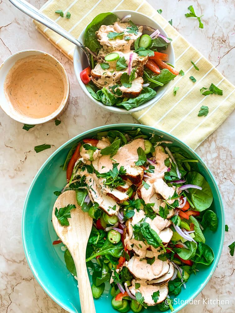 Grilled spicy chicken salad with yogurt dressing, spinach, cucumbers, and red onion in two bowls.