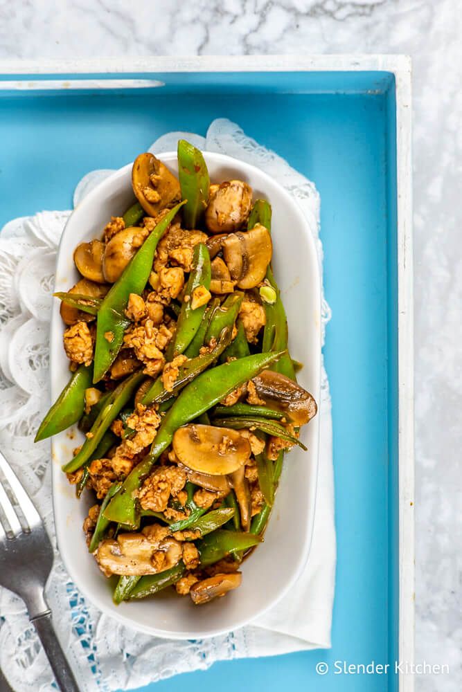 Turkey stirfry with mushrooms and green beans on a blue plate with chopsticks.