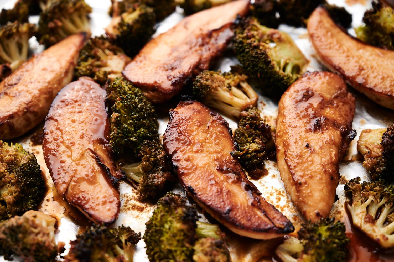 Spicy peanut chicken with broccoli florets in a sheet pan with caramelized charred edges.