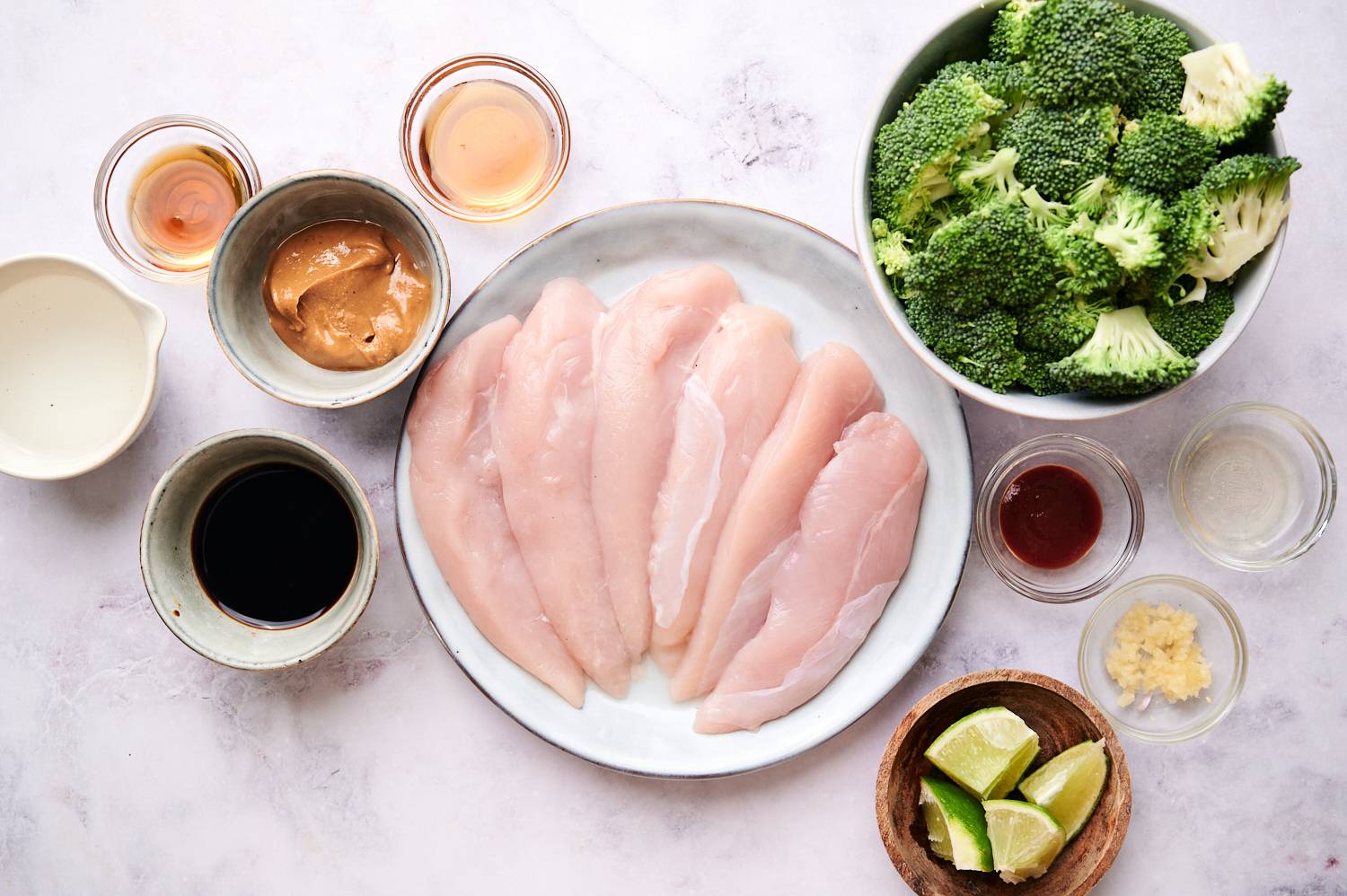 Ingredients for spicy peanut chicken and broccoli including chicken, broccoli, peanut butter, lime, garlic, ginger, and Sriracha.
