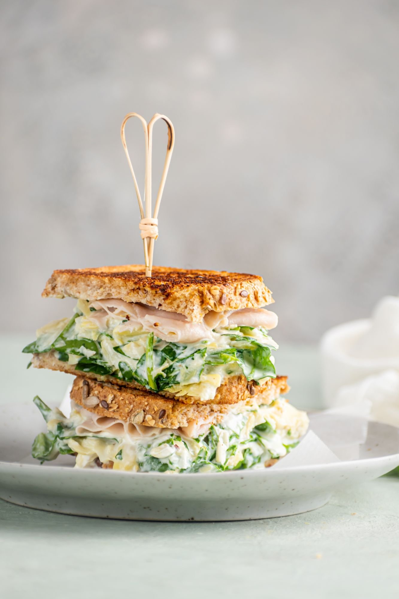 Spinach artichoke dip grilled cheese with whole wheat bread and turkey stacked on a plate.