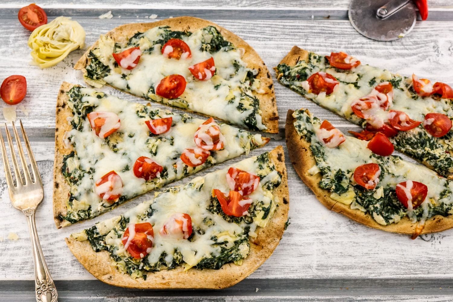 Spinach Artichoke Pizza on a thin flatbread with tomatoes.
