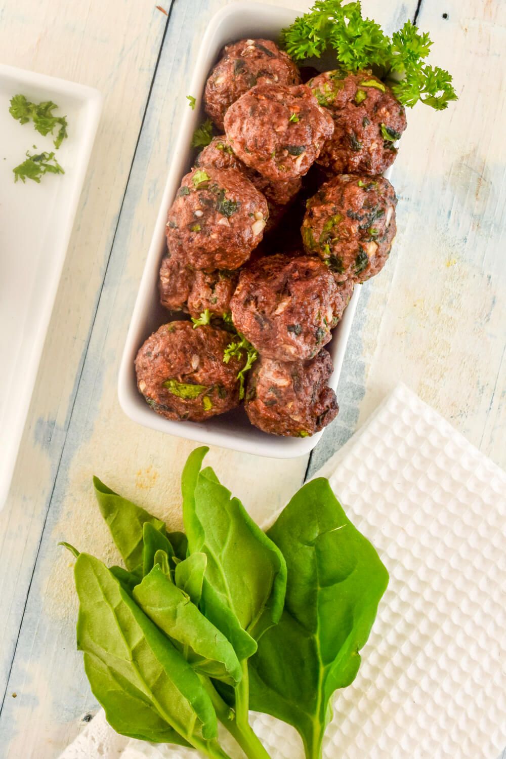 Spinach Meatballs on a white plate with fresh basil and wooden tongs.