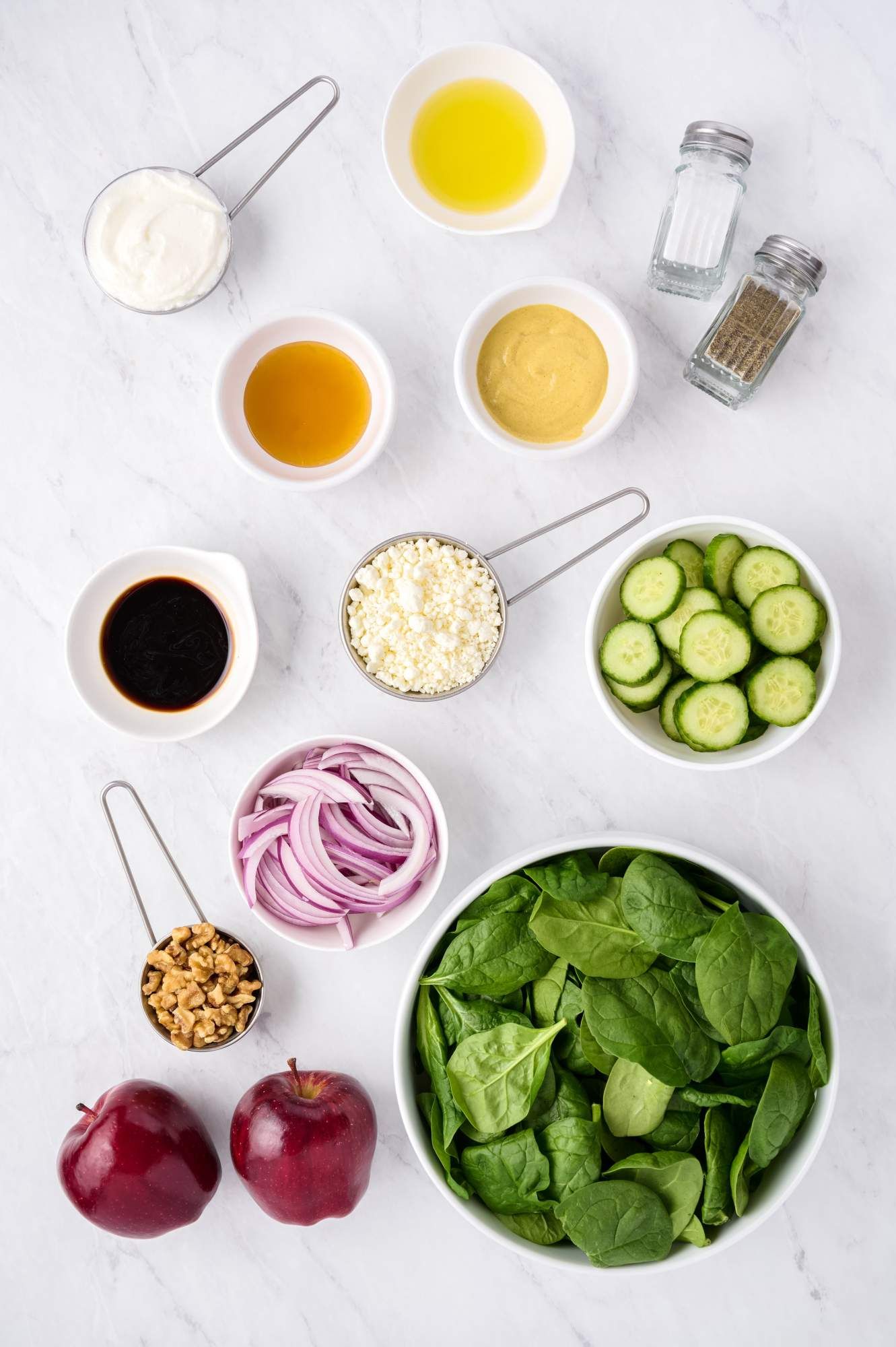 Ingredients for spinach salad including fresh baby spinach, red onions, cucumbers, apples, walnuts, goat cheese, and balsamic vinegar.