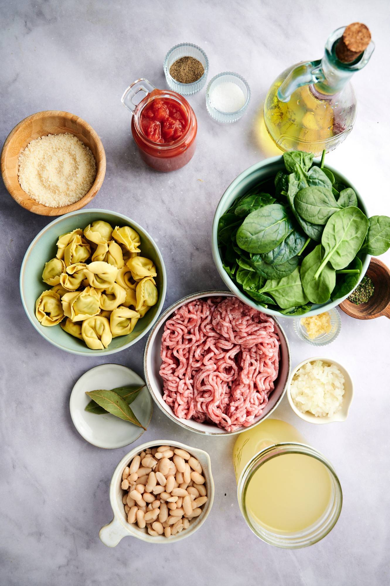 Ingredients for turkey tortellini soup with ground turkey, spinach, tortellini, garlic, onion, white beans, spices, Parmesan cheese, and tomatoes.