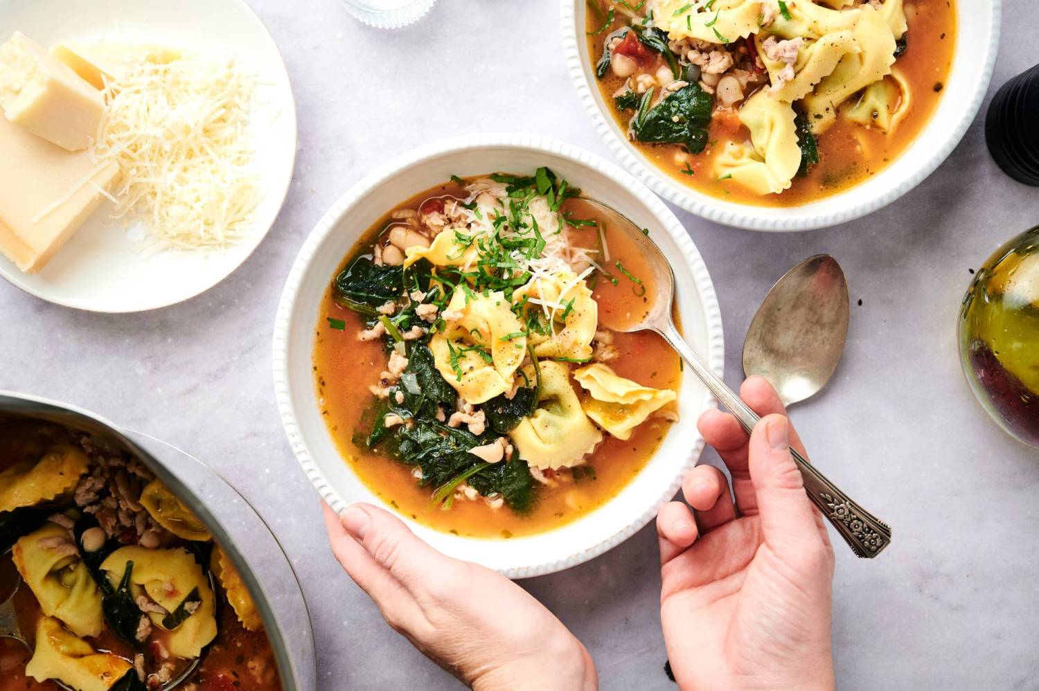 Spinach turkey tortellini soup with Parmesan cheese, white beans, tomatoes, and ground turkey in a bowl with a spoon.