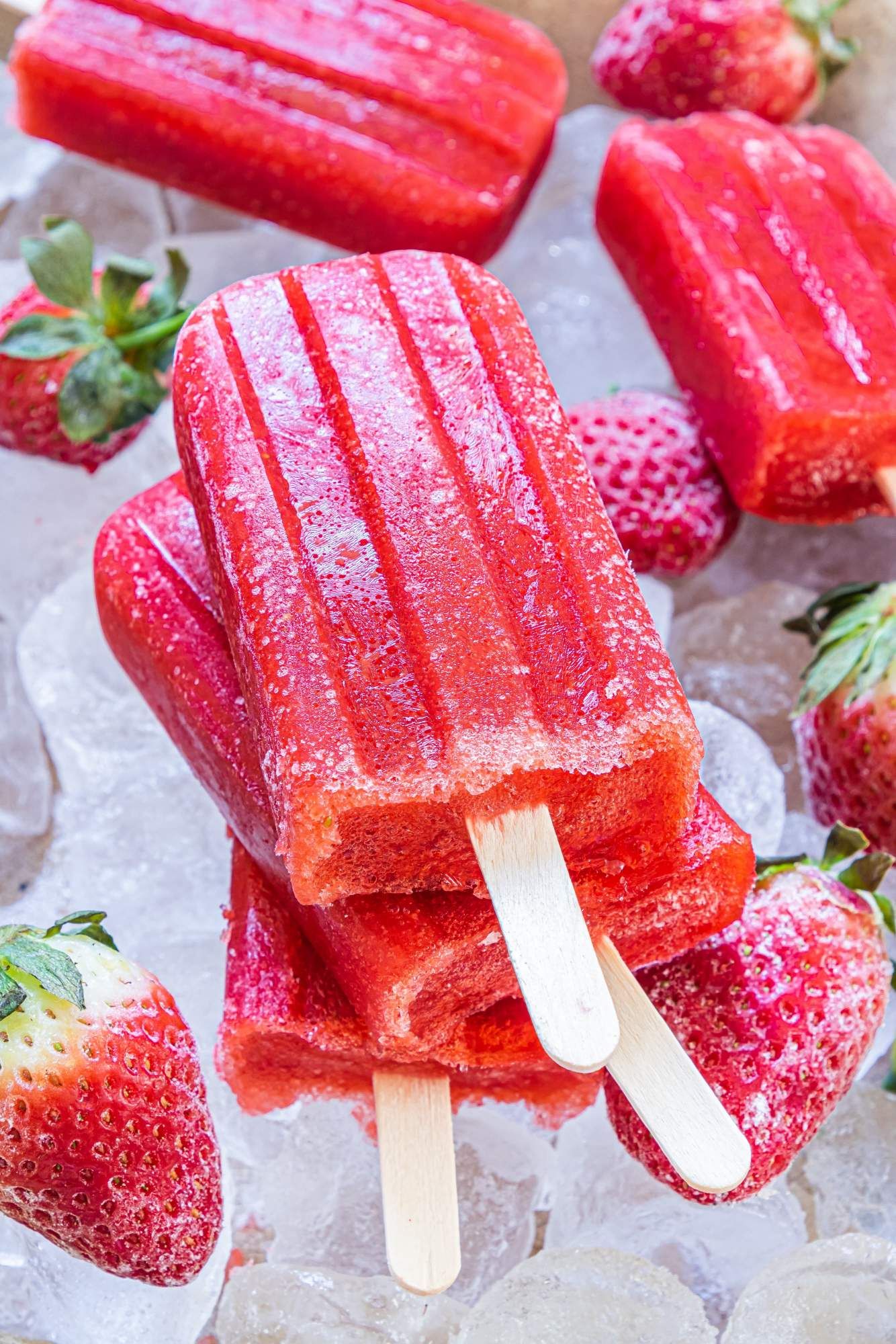 Homemade popsicles with strawberries, honey, and water stacked with strawberries on the side.