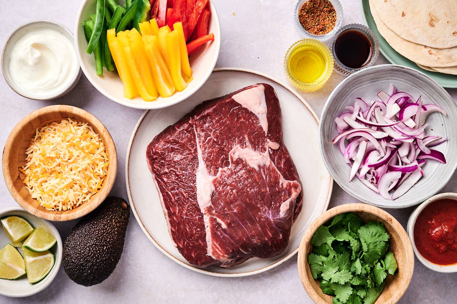 Ingredients for steak fajitas including flank steak, bell peppers, onions, fajita seasoning, olive oil, cilantro, tortillas, cheese, and salsa.