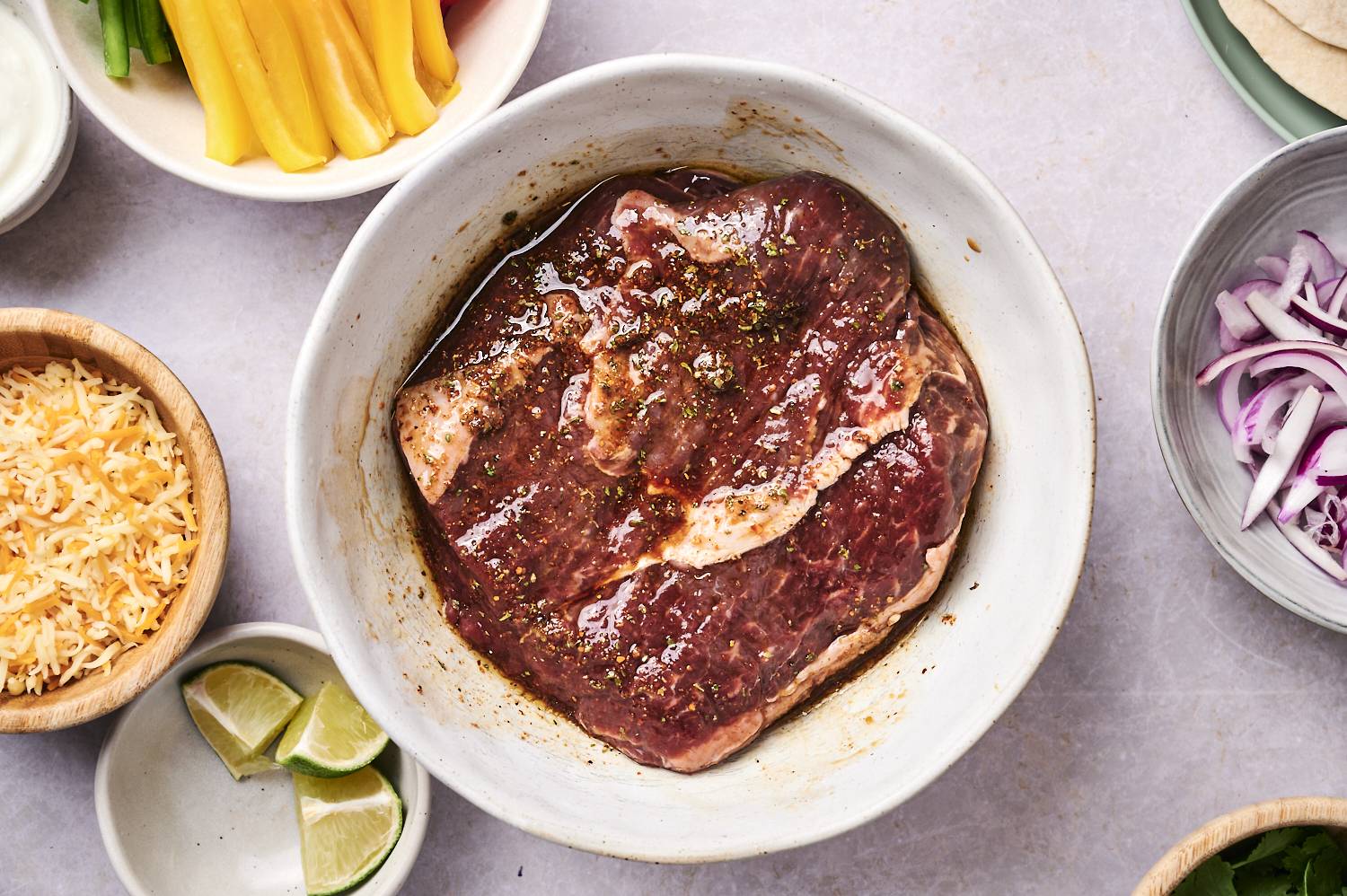 Flank steak marinating in lime juice and fajita seasoning in a large white bowl.