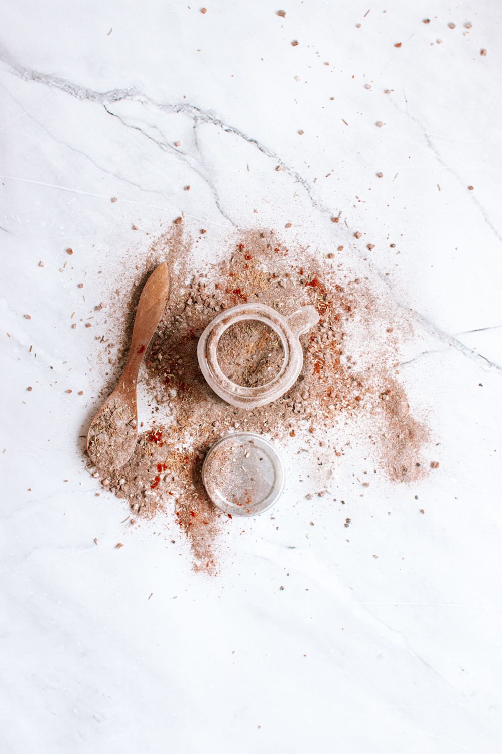 Steak spice blend mixed in a glass jar with some of the seasoning spilled on the side. 