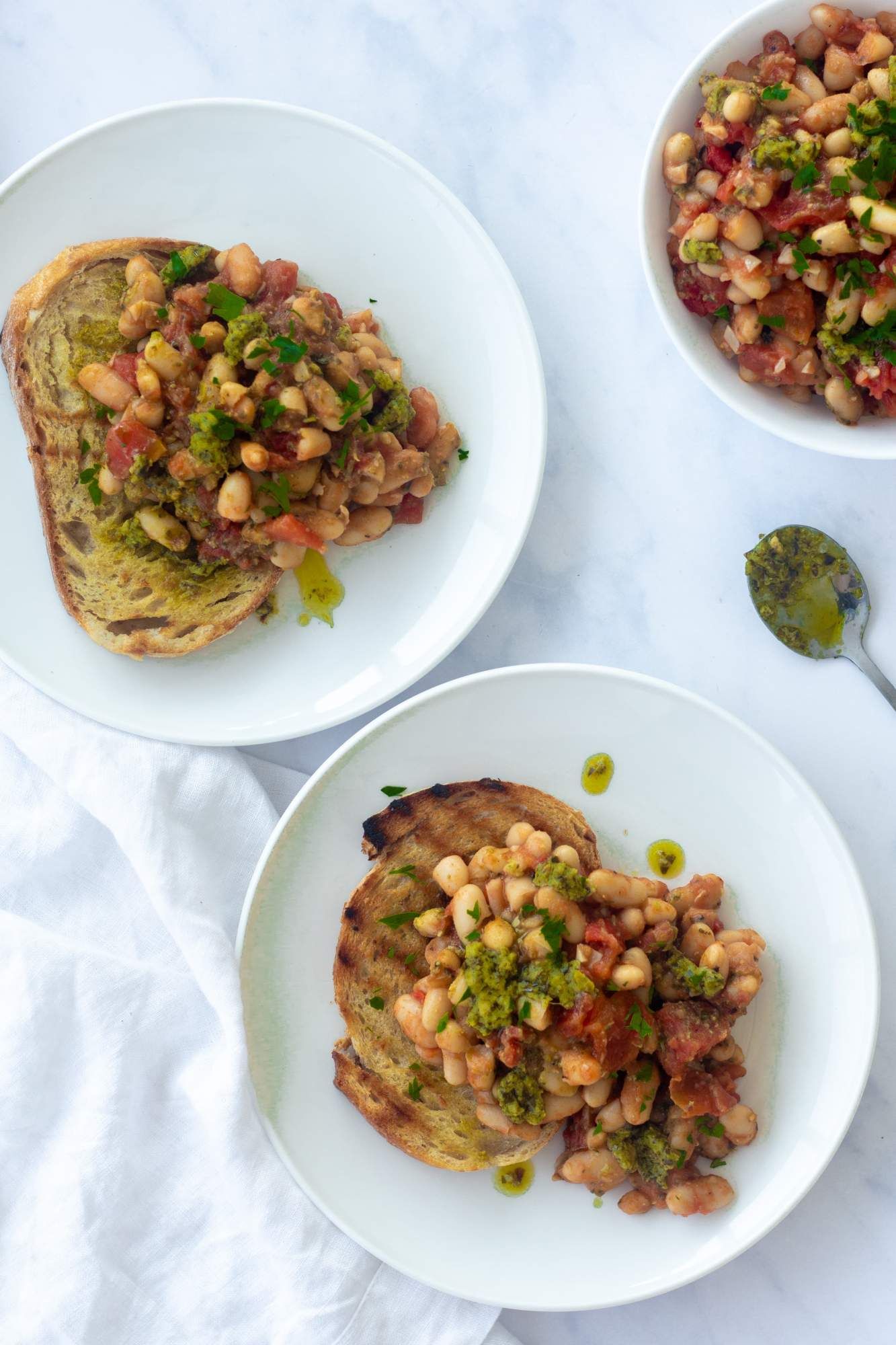 White beans stewed with tomatoes, garlic, and spices and then topped with pesto on two slices of toasted bread.