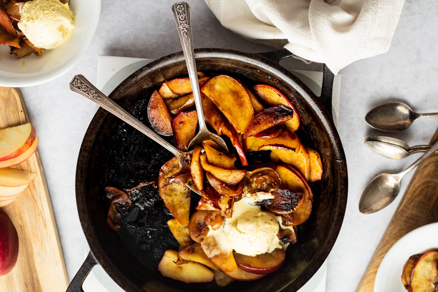 Apples in a pan being served with ice cream on top and spoons off to the side.