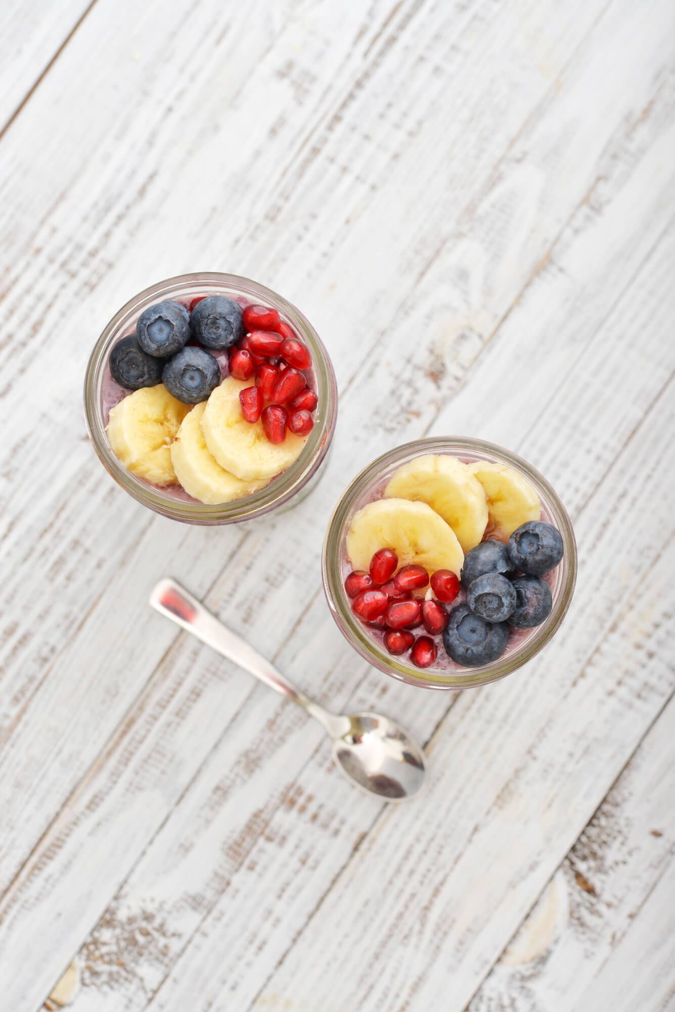 Strawberry chia seed pudding in two glass jars with bananas, blueberries, and pomegranate on top.