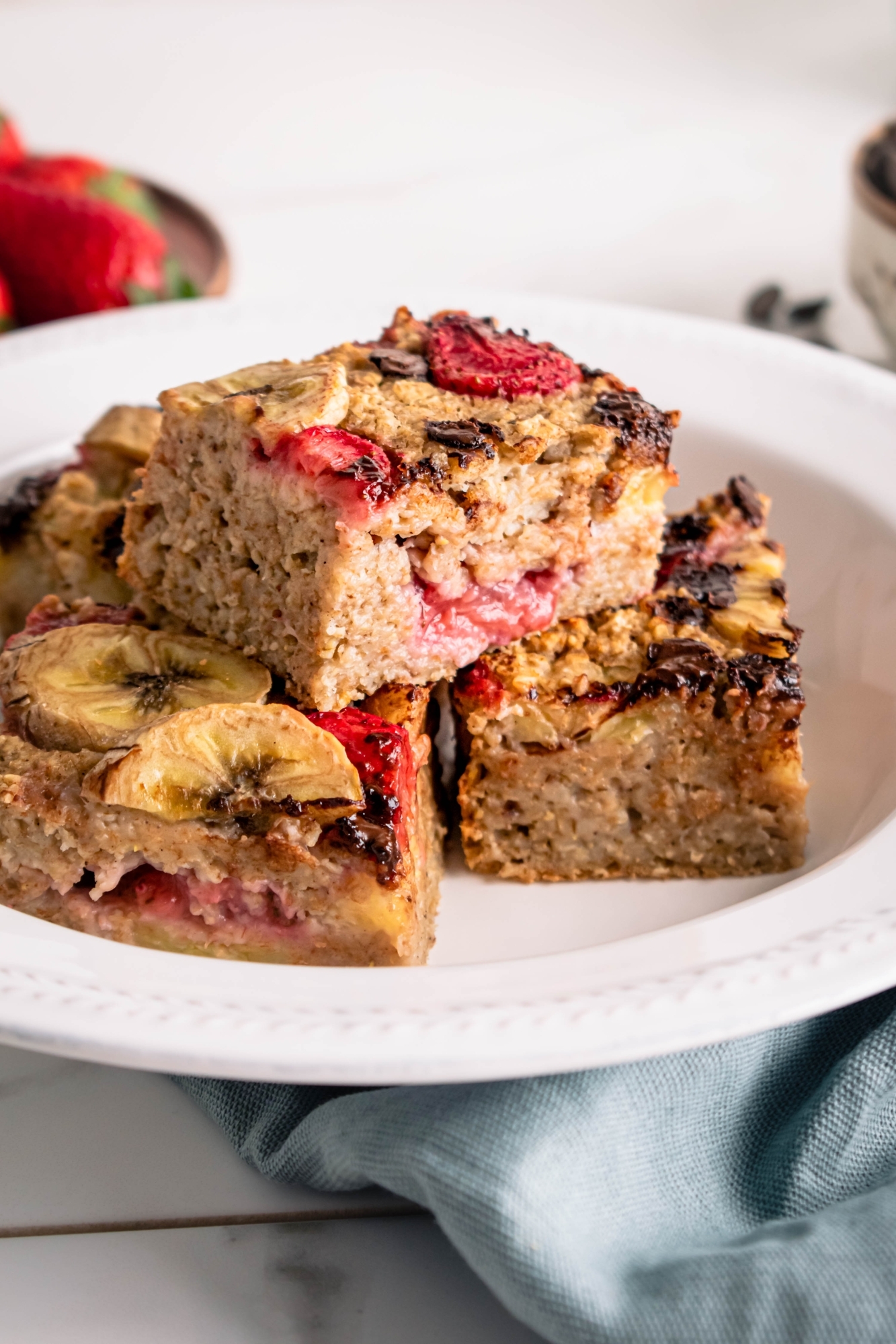 Strawberry baked oatmeal with banana and chocolate chips cut into squares and placed on a white plate.