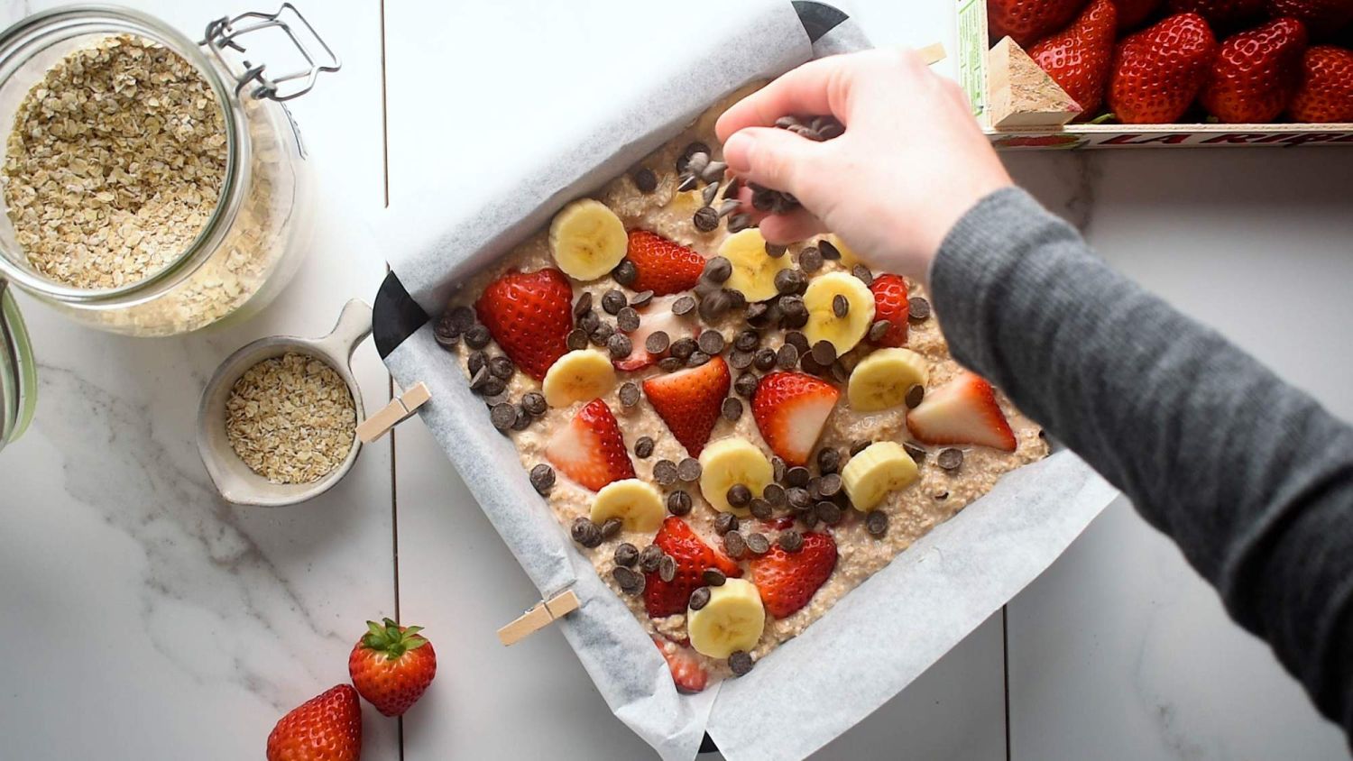 Chocolate chips being sprinlled on top of baked oatmeal with strawberries and bananas.
