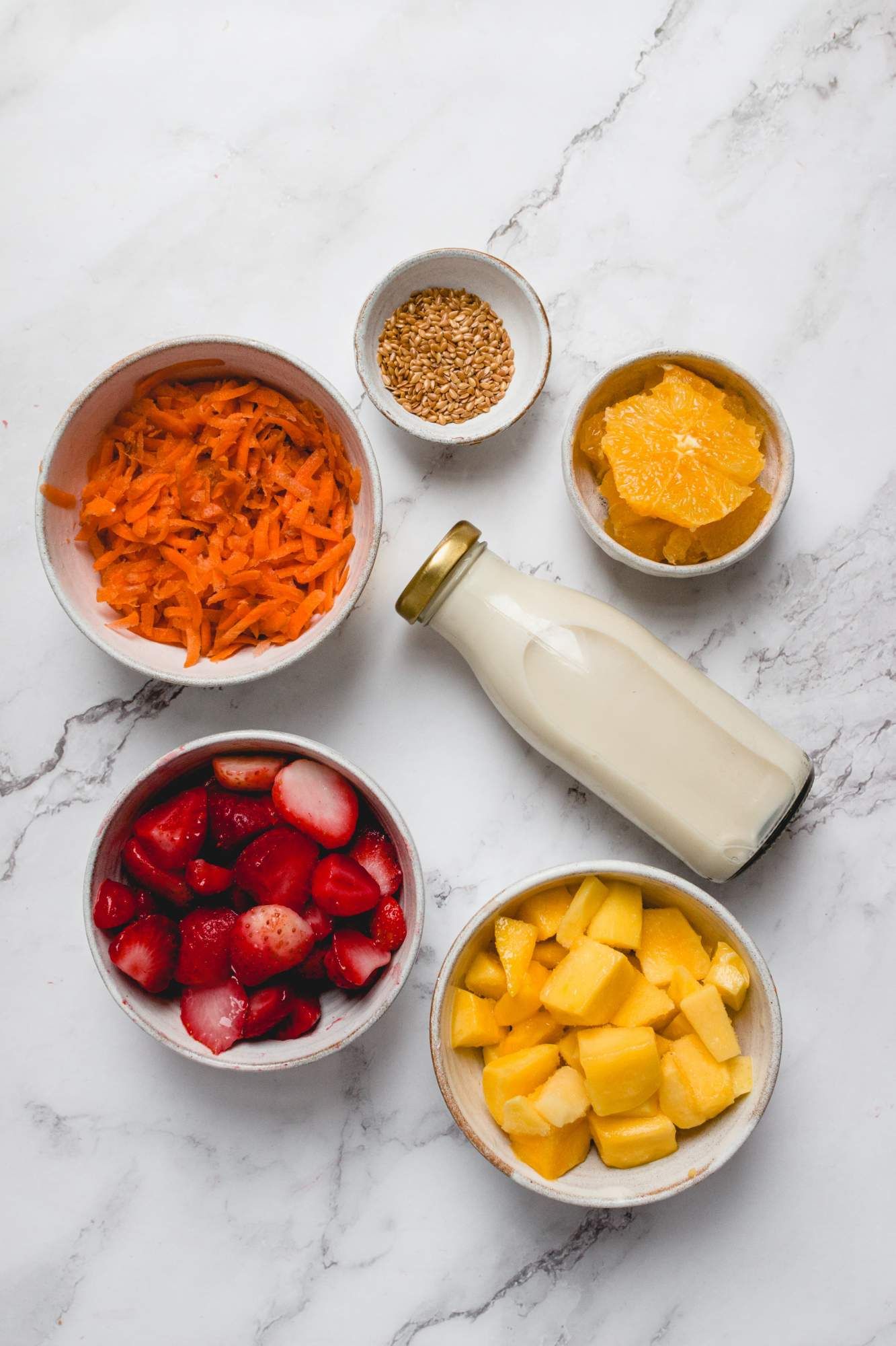 Mango strawberry smoothie ingredients including strawberries, mango chunks, carrots, flaxseeds, and almond milk.