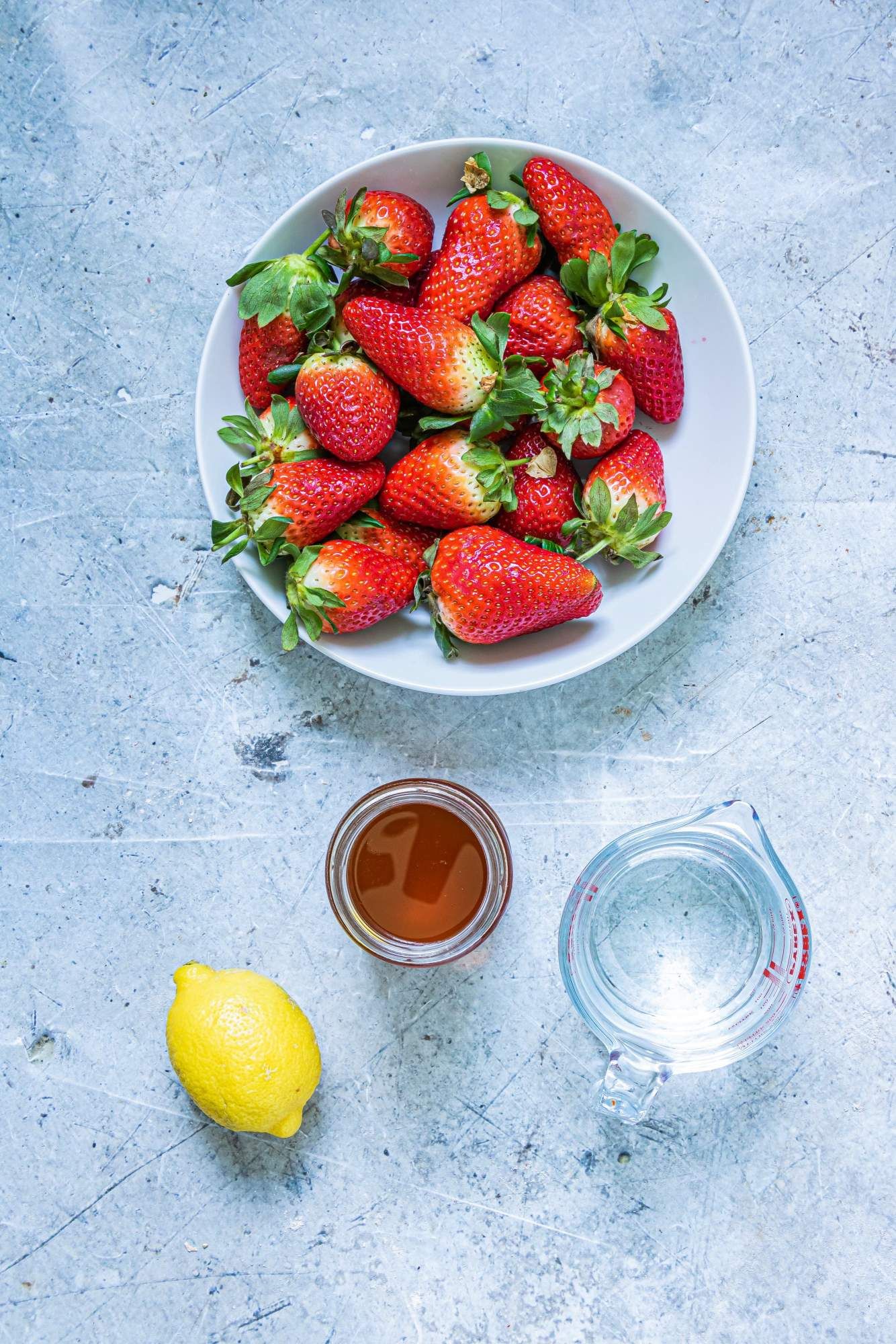 Ingredients to make strawberry popsicles including fresh strawberries, honey, water, and lemon juice.