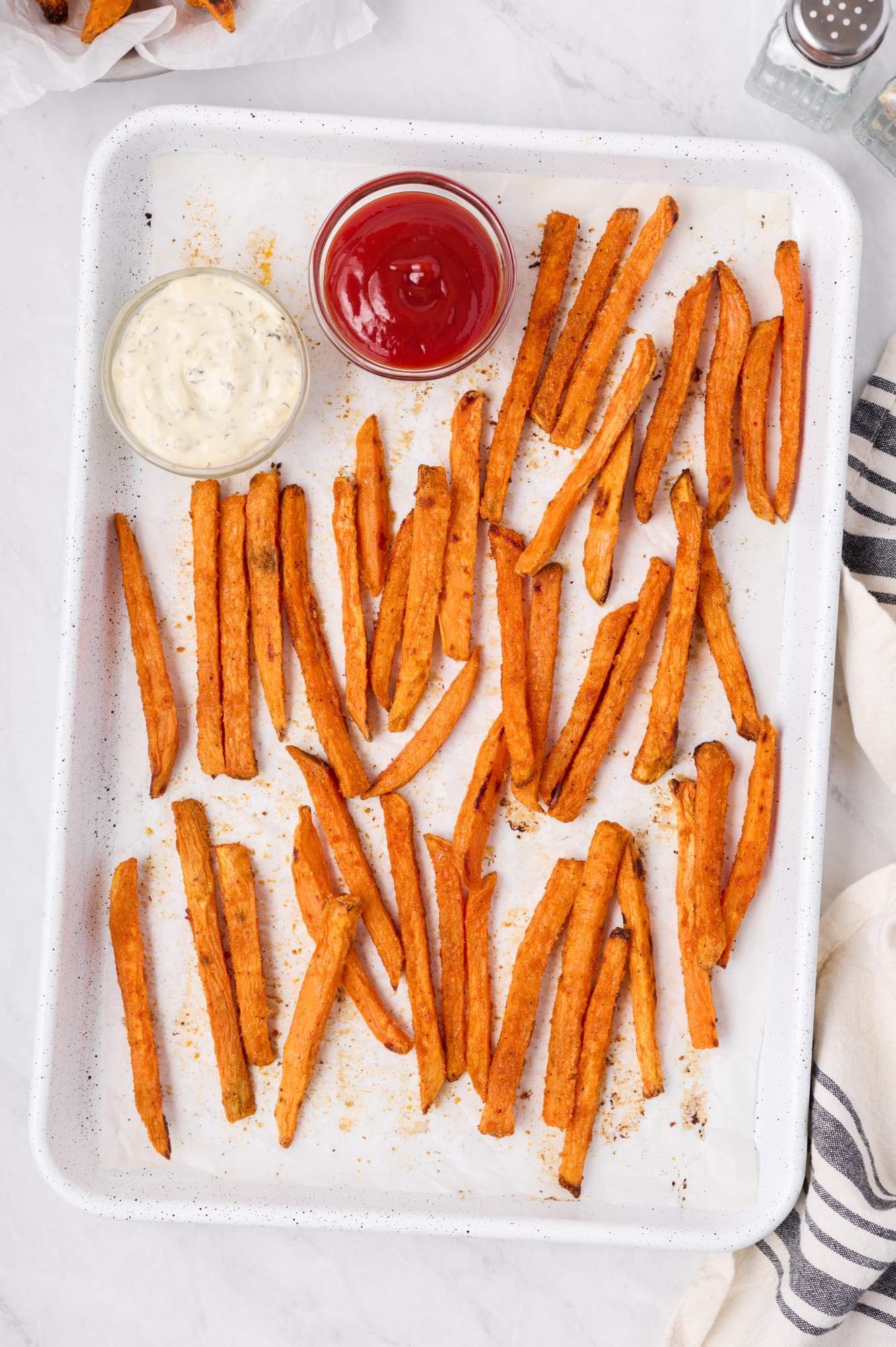 Crispy baked sweet potato french fries on a baking sheet with ketchup and ranch dip.