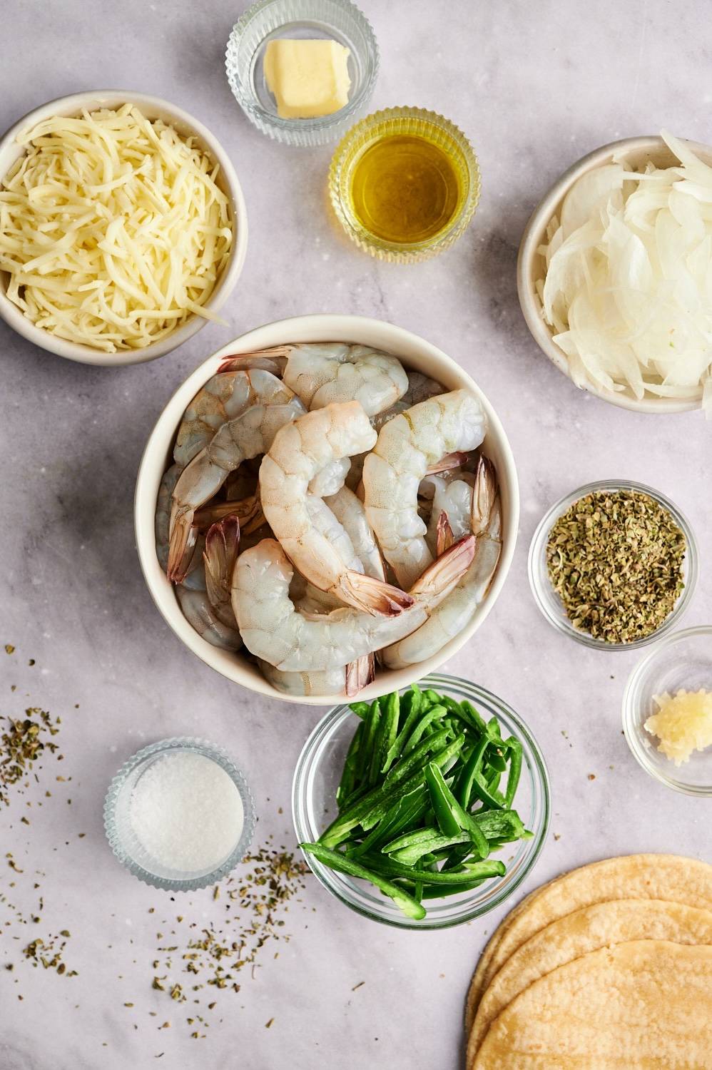 Ingredients for tacos gobernador including raw shrimp, shredded cheese, poblano peppers, onions, garlic, oregano, cilantro, and lime wedges.