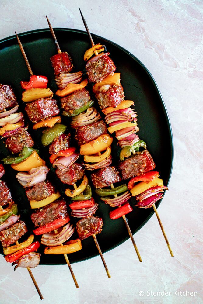 Beef kabobs in teriyaki sauce with bell peppers, red onions, and beef on a black plate.