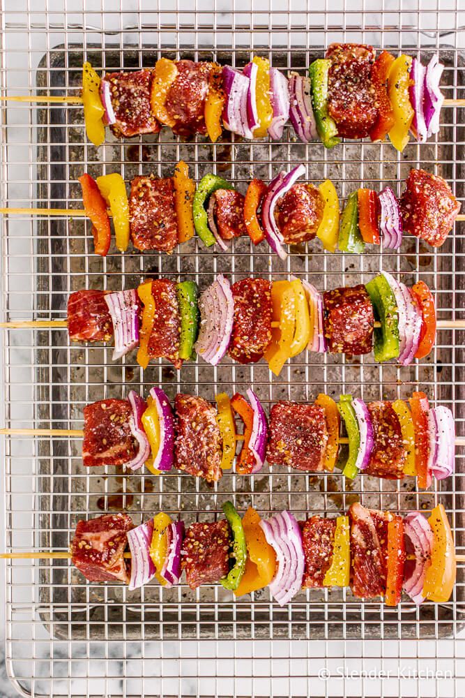 Teriyaki Steak Kabobs with bell peppers, red onions, and suace on skewers on a wire rack. 