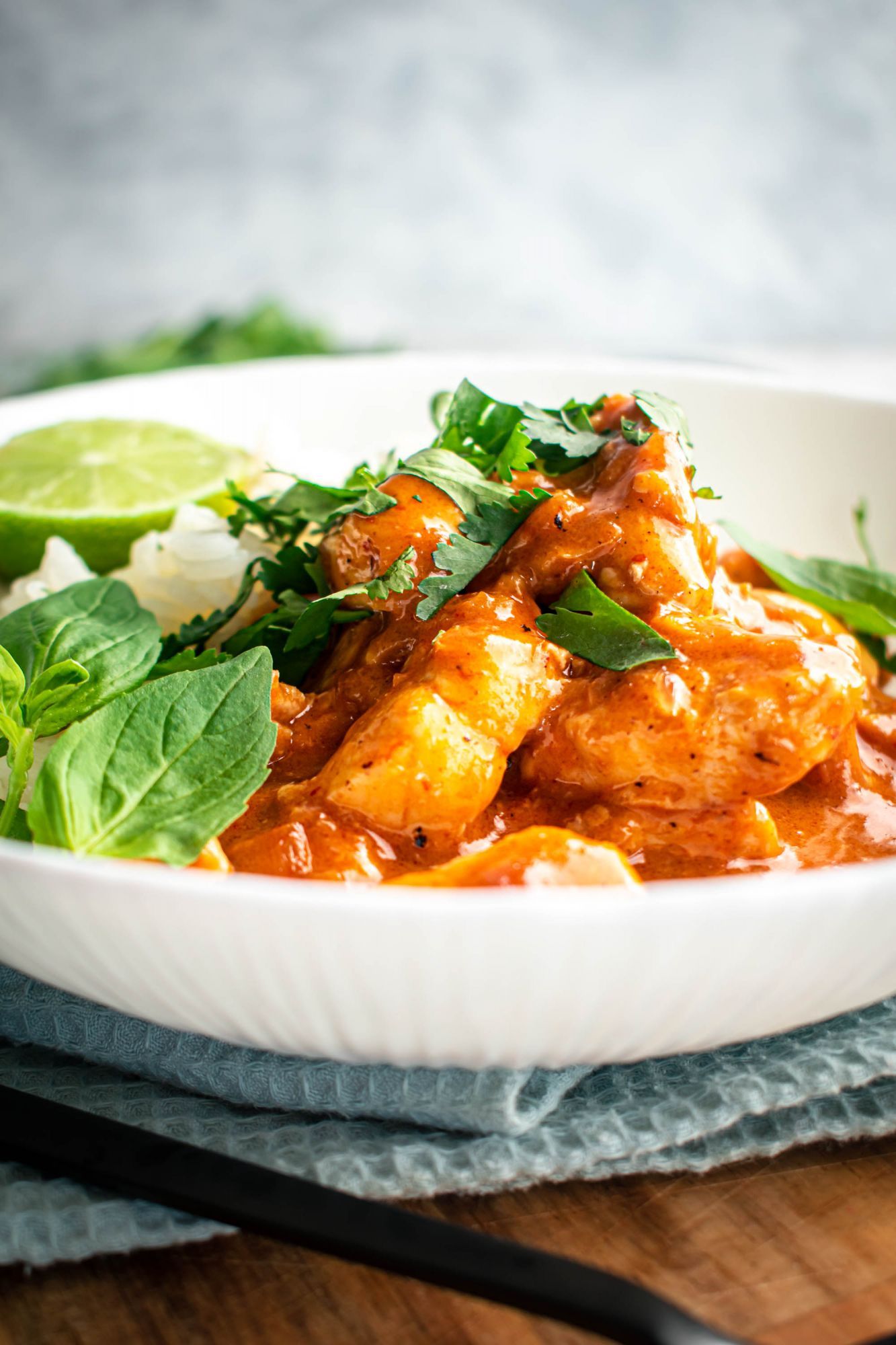 Thai curry chicken with creamy red curry sauce in a bowl with basil, cilantro, and steamed white rice.