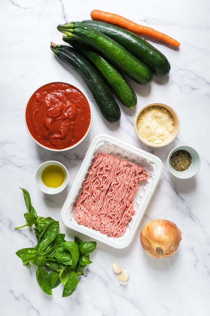 Ingredients to make tomato basil zucchini noodles with ground turkey including tomatoes, Parmesan cheese, basil, garlic, and onion.
