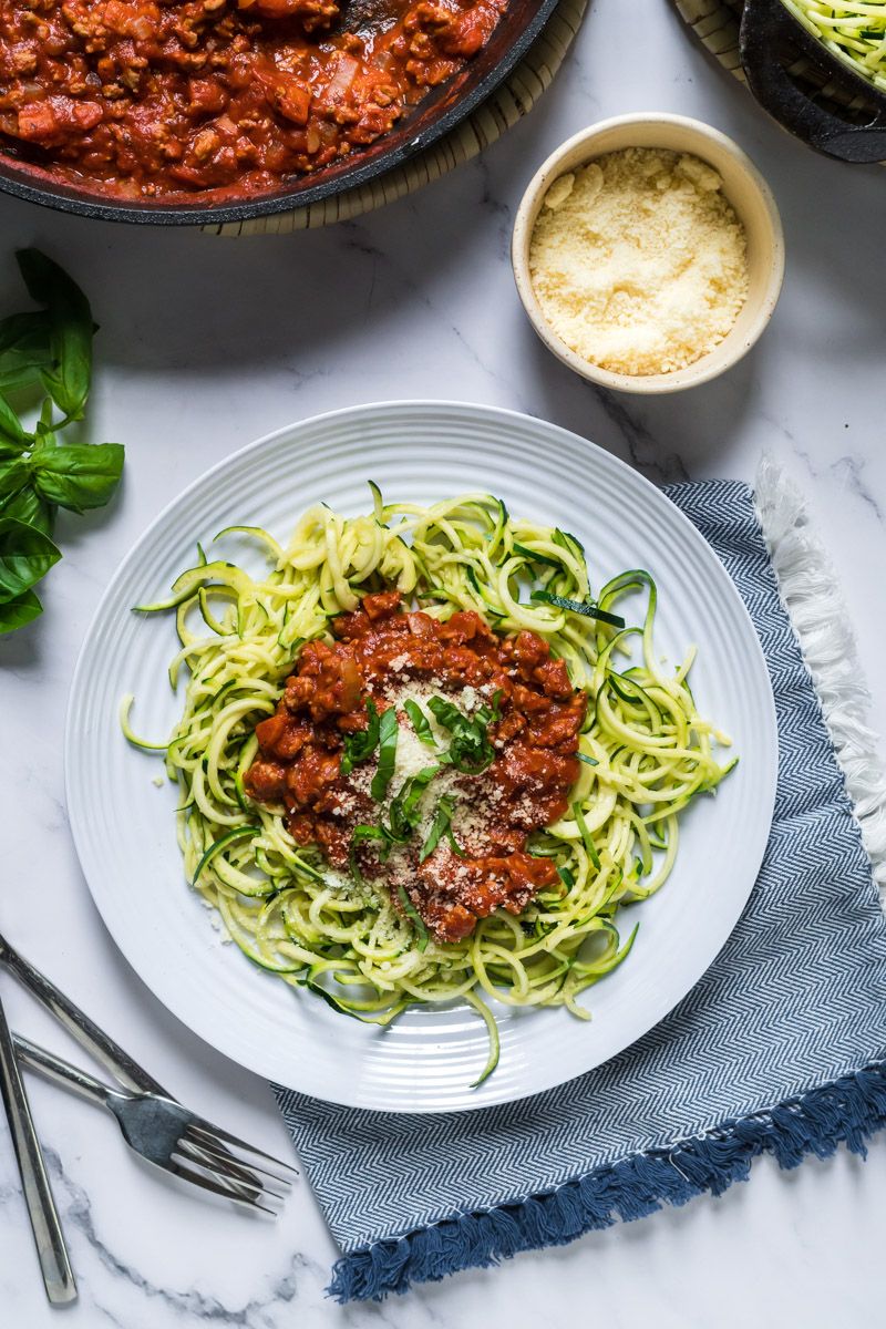 Zoodles with tomato basil ground turkey sauce on a plate with fresh basil and Parmesan cheese.