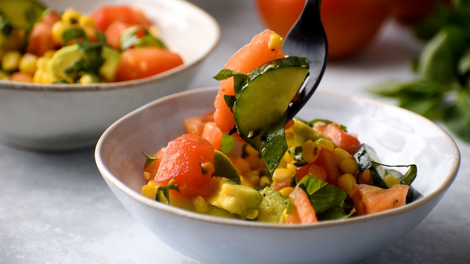 Tomatoes, cucumbers, corn, and avocado salad being picked up by a fork.