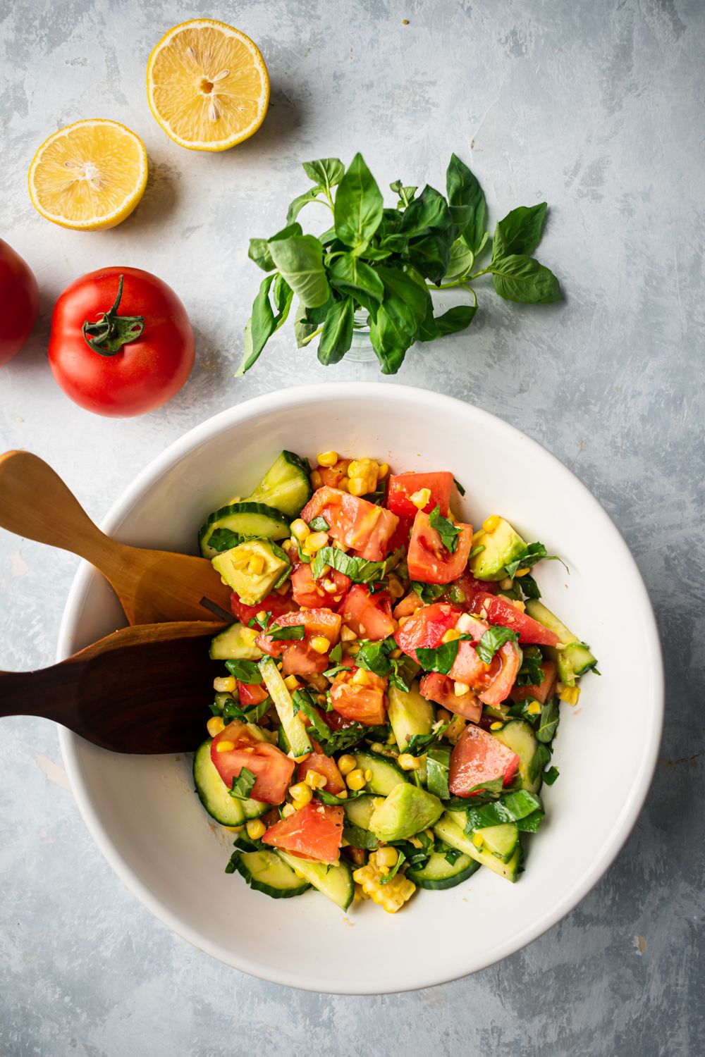 Cucumber, tomato, and avocado salad with fresh basil and lemons in a bowl.