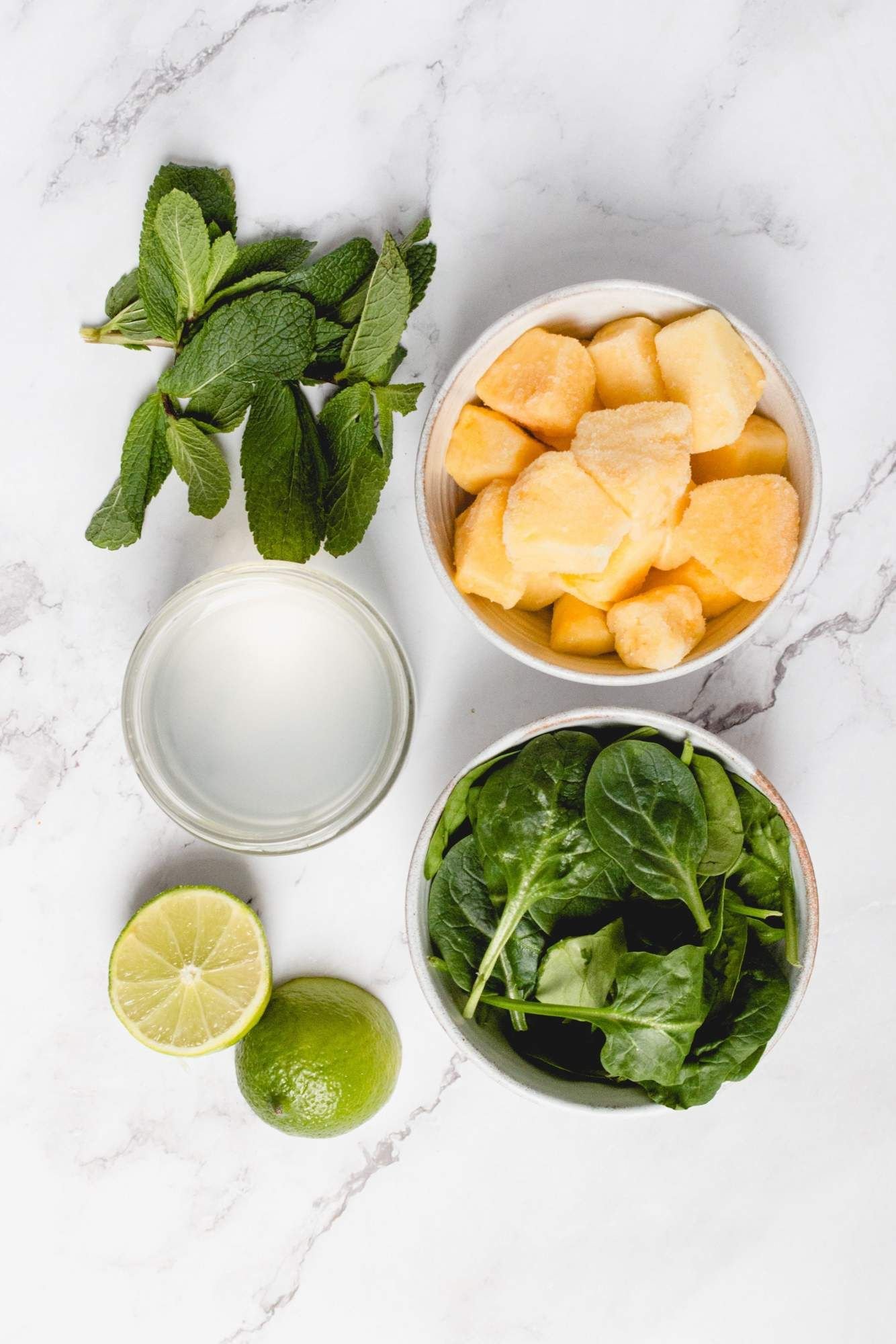 Ingredients for pineapple smoothies including frozen pineapple, spinach, mint, lime juice, and coconut water.