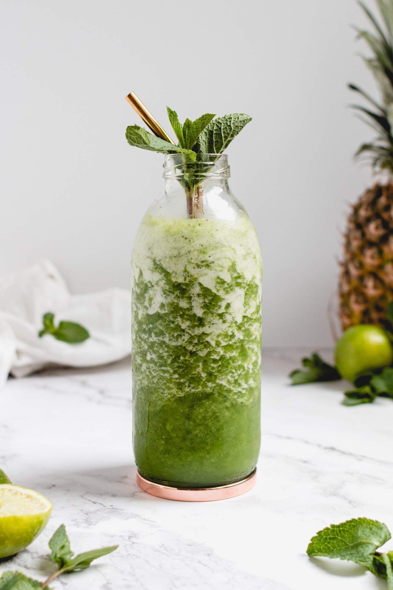 Tropical pineapple and mint mojito smoothie in a jar with mint sprigs and a gold straw.