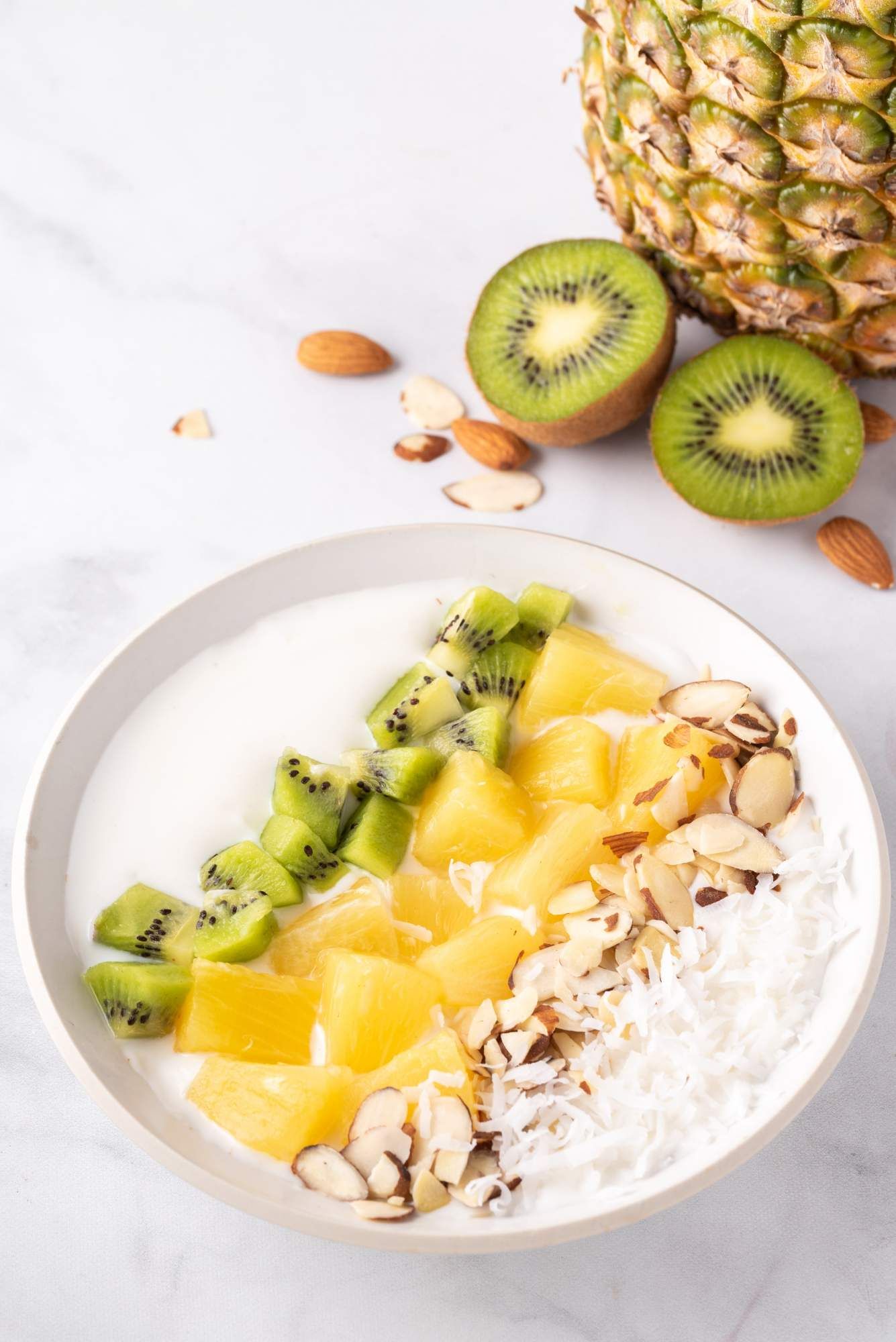 Tropical coconut yogurt bowl with pineapple, sliced kiwi, sliced almonds, and shredded coconut layered in a bowl.