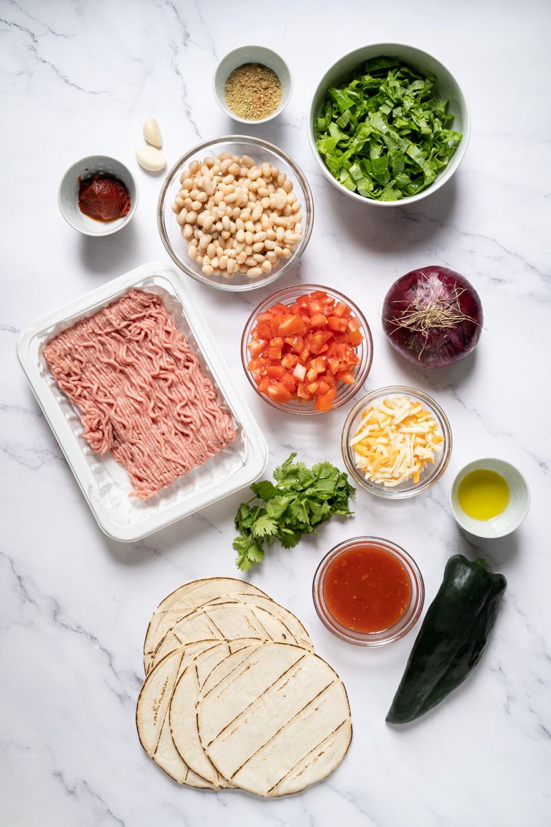 Ingredients for turkey poblano tostadas including ground turkey, poblano peppers, beans, lettuce, tomatoes, and shredded cheese.