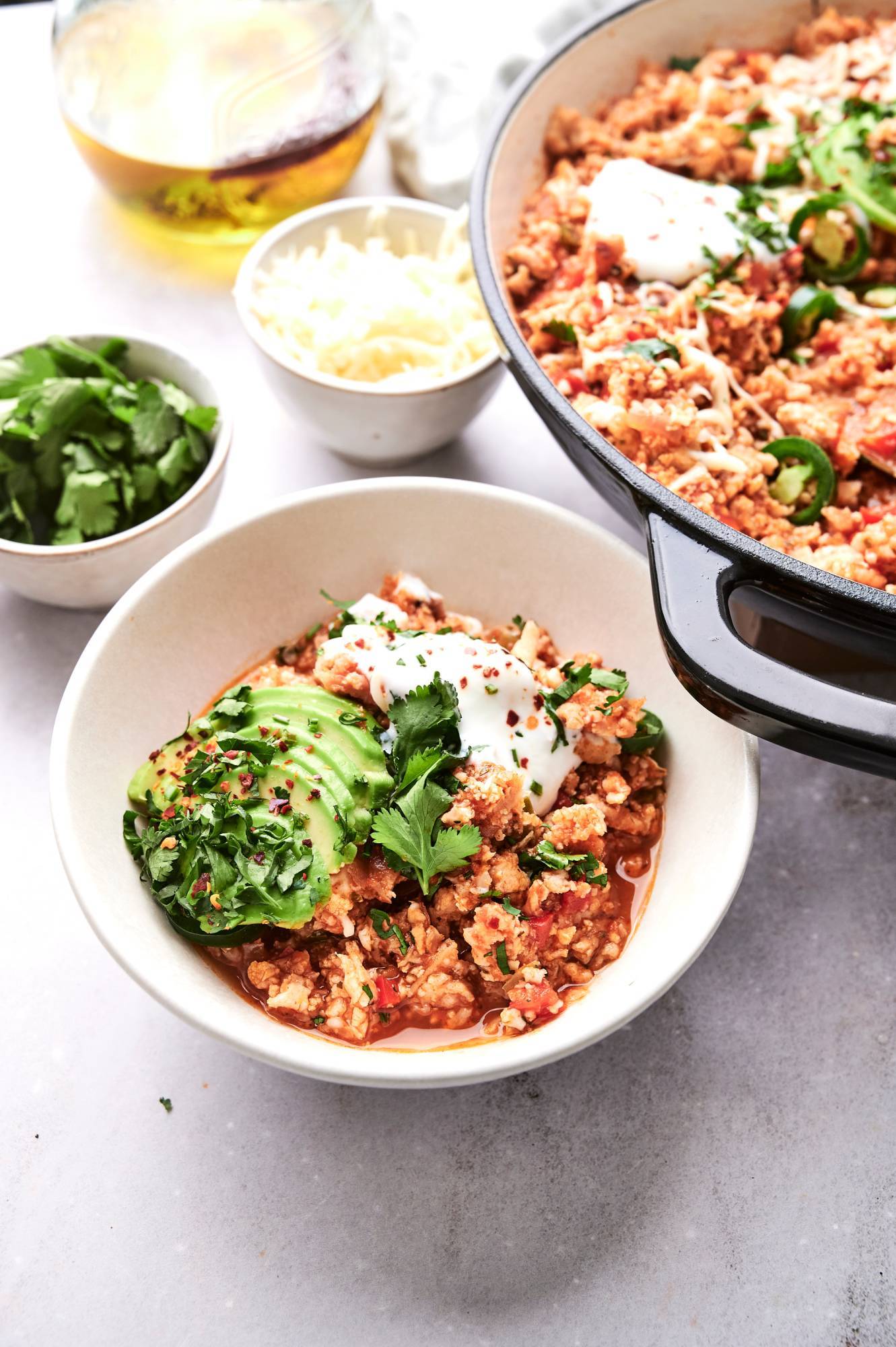 Cauliflower rice turkey taco skillet in a bowl with sour cream, jalapenos, cilantro, and shredded cheese.