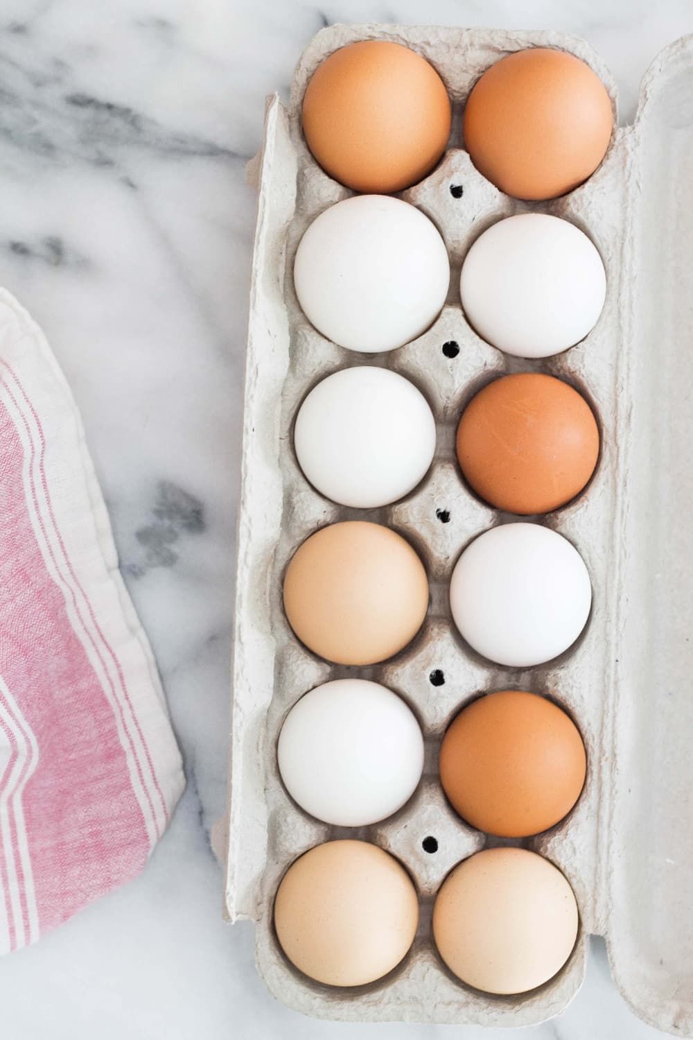Different types of eggs in a carton including white, brown, and tan.