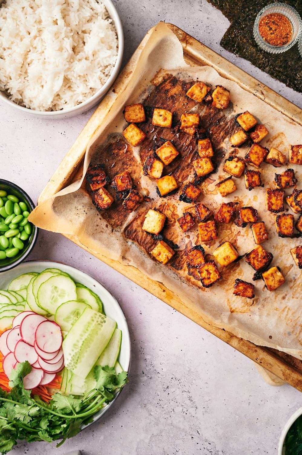 Crispy tofu on a baking sheet with vegetables on the side for sushi bowls.