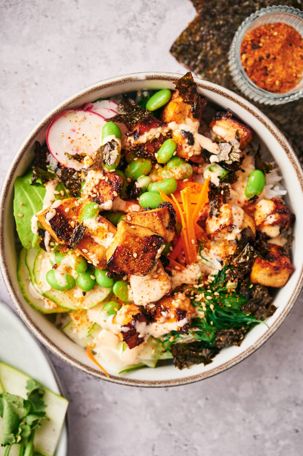 Tofu sushi bowls with cripsy tofy, carrots, seaweed, edamame, avocado, cucumbers, and sesame seeds served over white rice.
