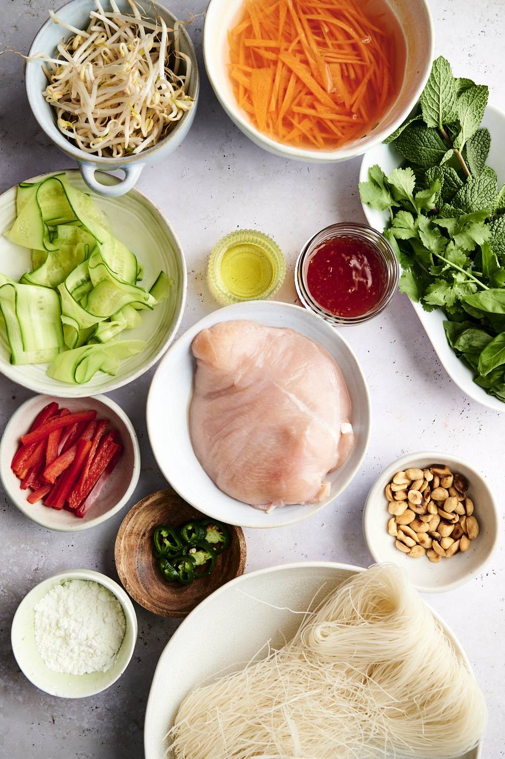 Ingredients for vietnamese vermicelli noodle bowls including chicken, noodles, cucumber, carrots, bean sprouts, peanuts, and fresh herbs.