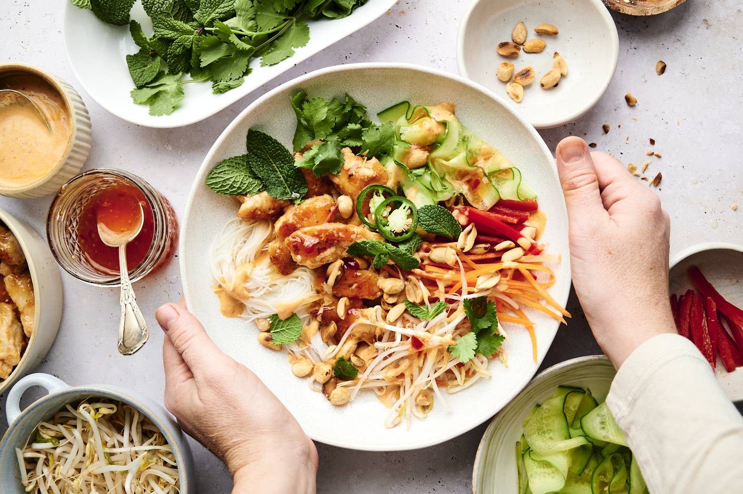 Vermicelli noodles, chicken, carrots, bean sprouts, herbs, and jalapenos in a bowl with peanuts and extra sauce on the side.