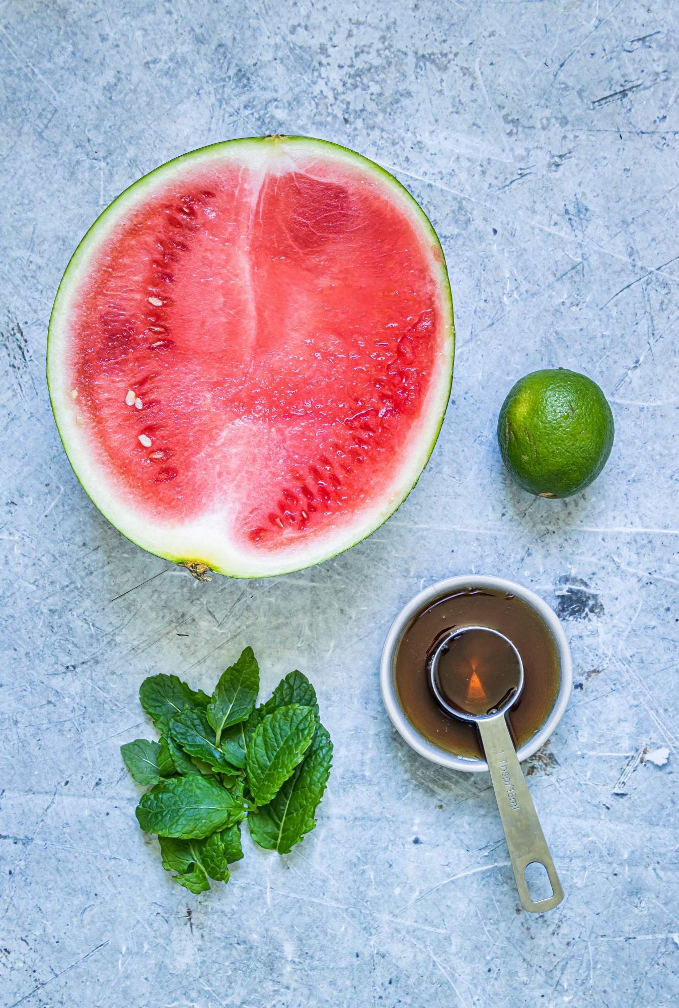 Ingredients for watermelon popsicles including fresh watermelon, honey, mint, and lime juice.